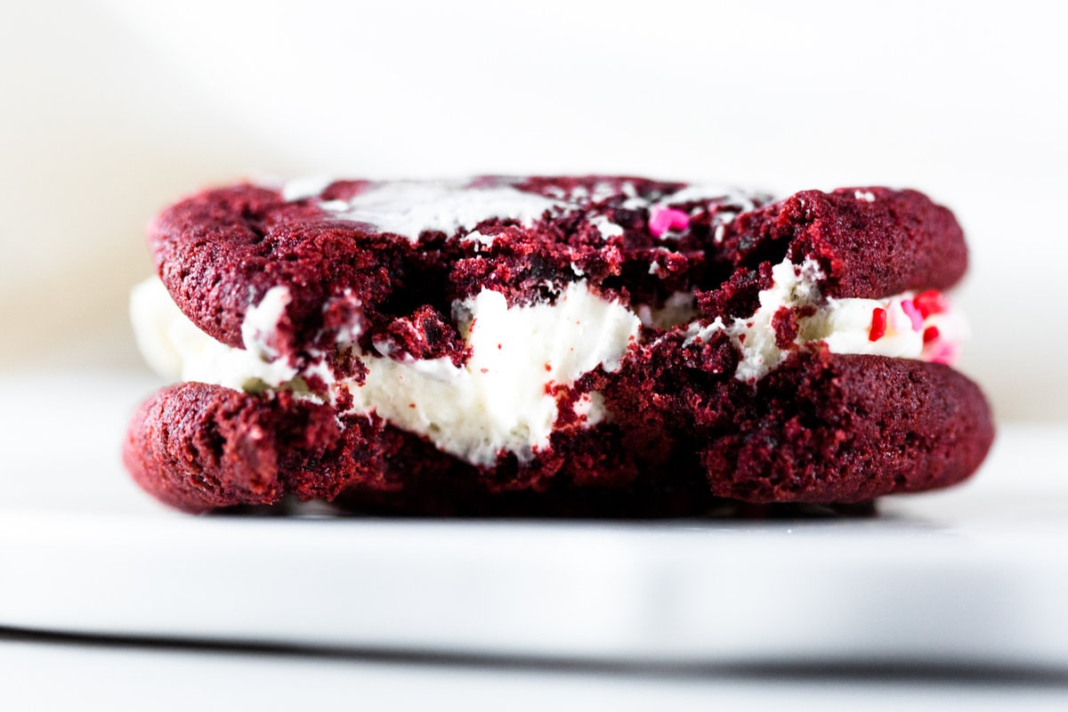 Delicious and chewy Vegan Red Velvet Cookies sandwiched with a yummy Cream Cheese Frosting. Think Red Velvet Cake, but in a convenient cookie form! #redvelvet #cookies #veganredvelvet #vegancookies #cheesecake #creamcheese #icing #dairyfree #eggless #cake #simple #easy #baking