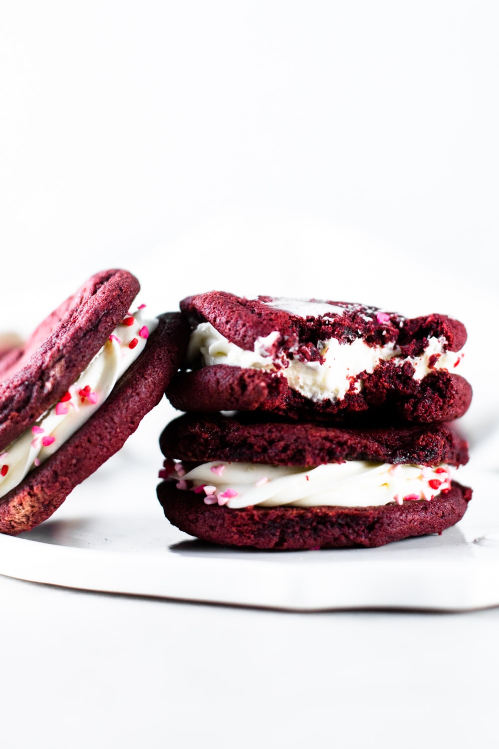 Delicious and chewy Vegan Red Velvet Cookies sandwiched with a yummy Cream Cheese Frosting. Think Red Velvet Cake, but in a convenient cookie form! #redvelvet #cookies #veganredvelvet #vegancookies #cheesecake #creamcheese #icing #dairyfree #eggless #cake #simple #easy #baking
