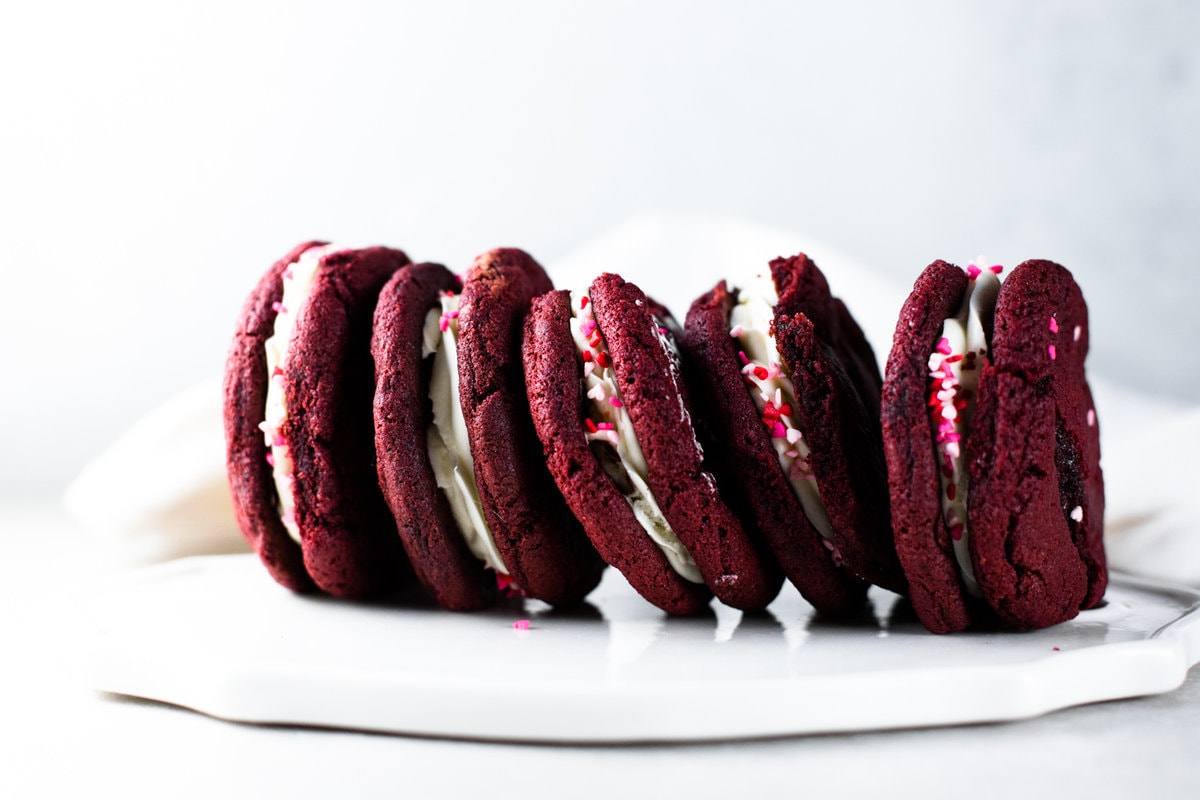 Delicious and chewy Vegan Red Velvet Cookies sandwiched with a yummy Cream Cheese Frosting. Think Red Velvet Cake, but in a convenient cookie form! #redvelvet #cookies #veganredvelvet #vegancookies #cheesecake #creamcheese #icing #dairyfree #eggless #cake #simple #easy #baking